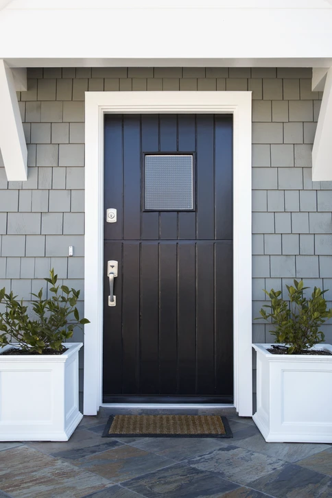 Entrée extérieure résidentielle avec porte d'entrée noire à panneaux verticaux et vitre dépolie carrée